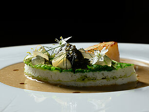 Gourmet-Meeresfrüchtegericht mit Kaviar, essbaren Blüten und Mousse auf weißem Teller mit Sauce