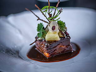 Gourmet-Rindfleischgericht mit reichhaltiger Soße, garniert mit Kräutern und Gemüse auf elegantem weißen Teller
