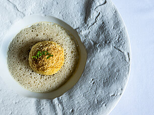 Gourmet dish with a golden croquette on creamy sauce garnished with herbs