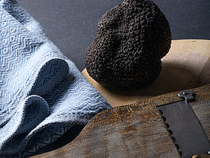 Ganze schwarze Trüffel mit Trüffelhobel und blauem Tuch auf dunkler Oberfläche